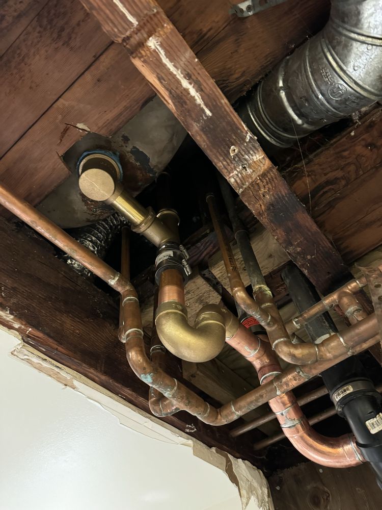Plumber inspecting drain and waste pipe routing under a sink